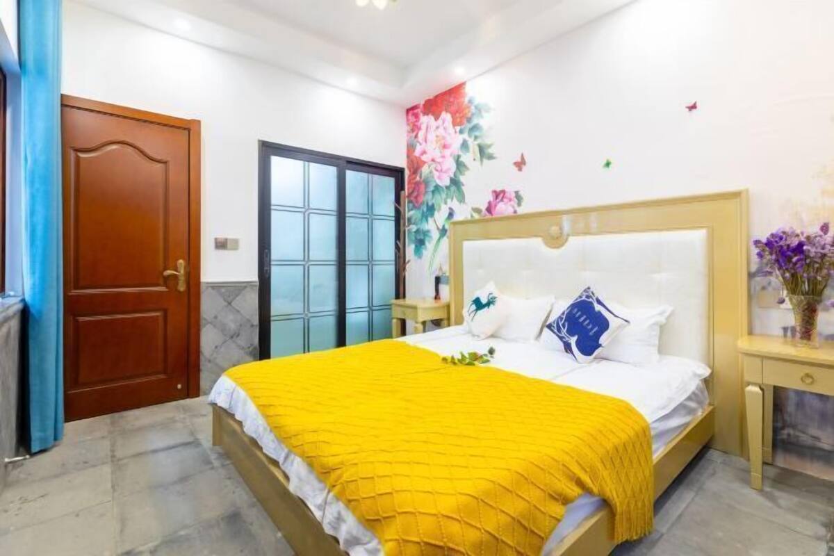 A bedroom with a bed, a wooden door, a window, and a wall with floral decorations.