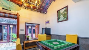 Een kamer met een tafel met groene vilt voor een spel, gele stoelen, een klassieke plafondventilator en een schilderij aan de muur.