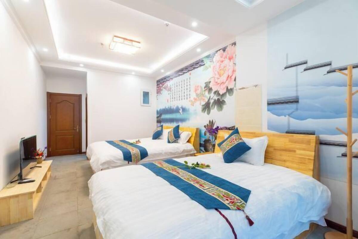 A hotel room with two beds, a wooden headboard, a mural on the wall, and a desk with a computer.
