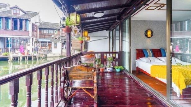 Un balcon en bois avec un lit, des plantes en pot et une vue sur des bâtiments traditionnels.