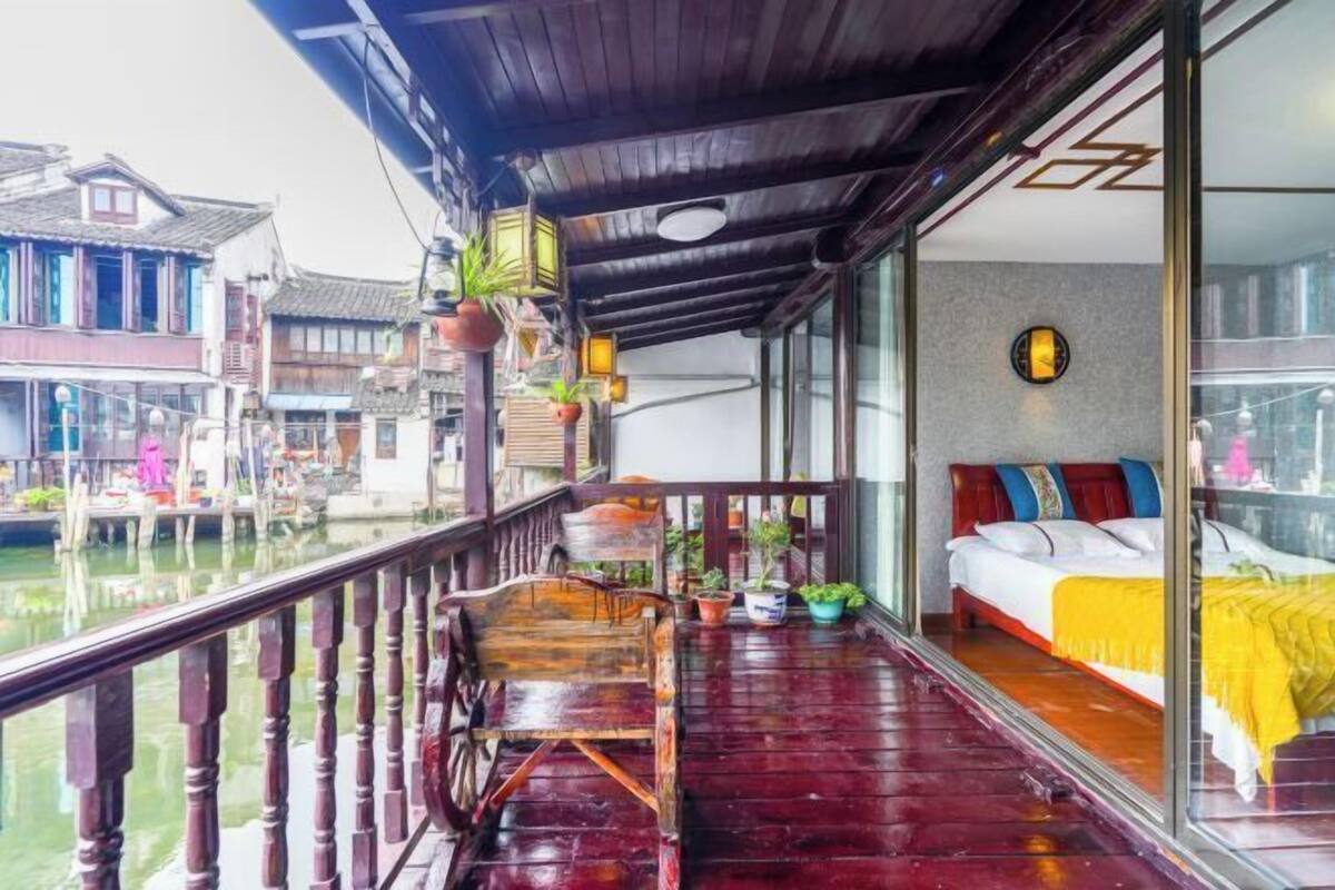 A wooden balcony with a bed, potted plants, and a view of traditional buildings.