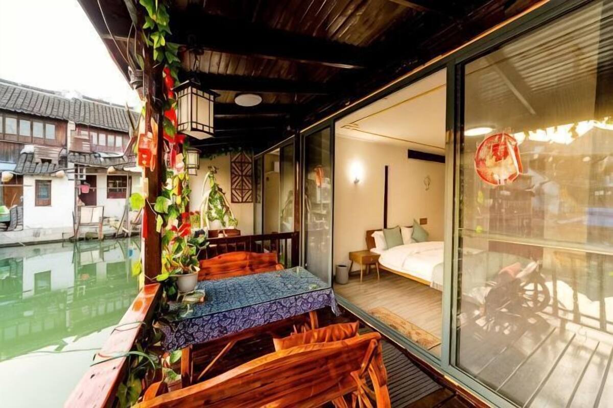 A traditional wooden balcony with a table and chairs, a view of a water body, and a glimpse of a traditional building in the background.