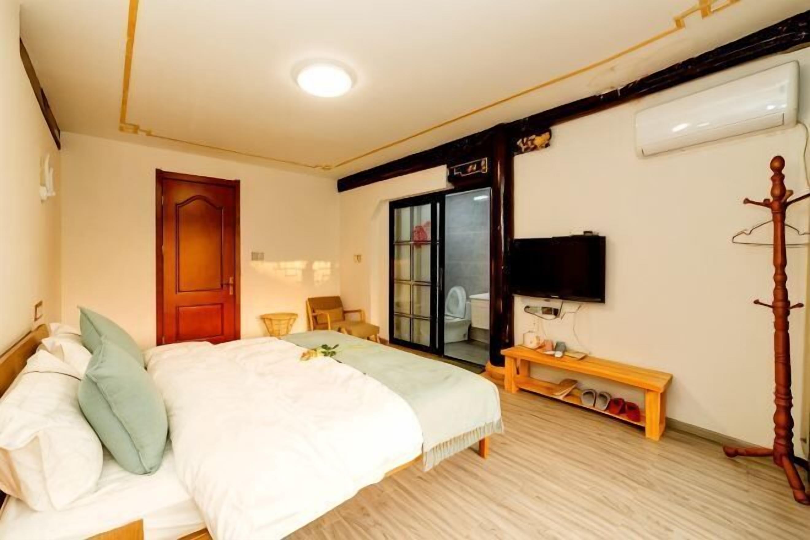 Un dormitorio con cama, televisor, perchero y banqueta.
