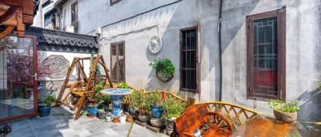 A courtyard with a wooden swing set, a table with a potted plant, and a traditional building with a tiled roof.