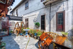 A courtyard with a wooden swing set, a table with a potted plant, and a traditional building with a tiled roof. - Zhouzhuang Linshui Renjia Inn (Kunshan)