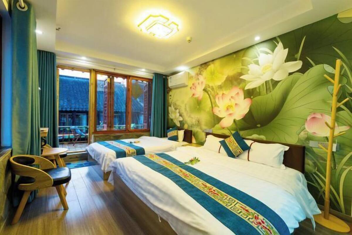 A hotel room with two beds, a view of a traditional building, and a mural of flowers on the wall.