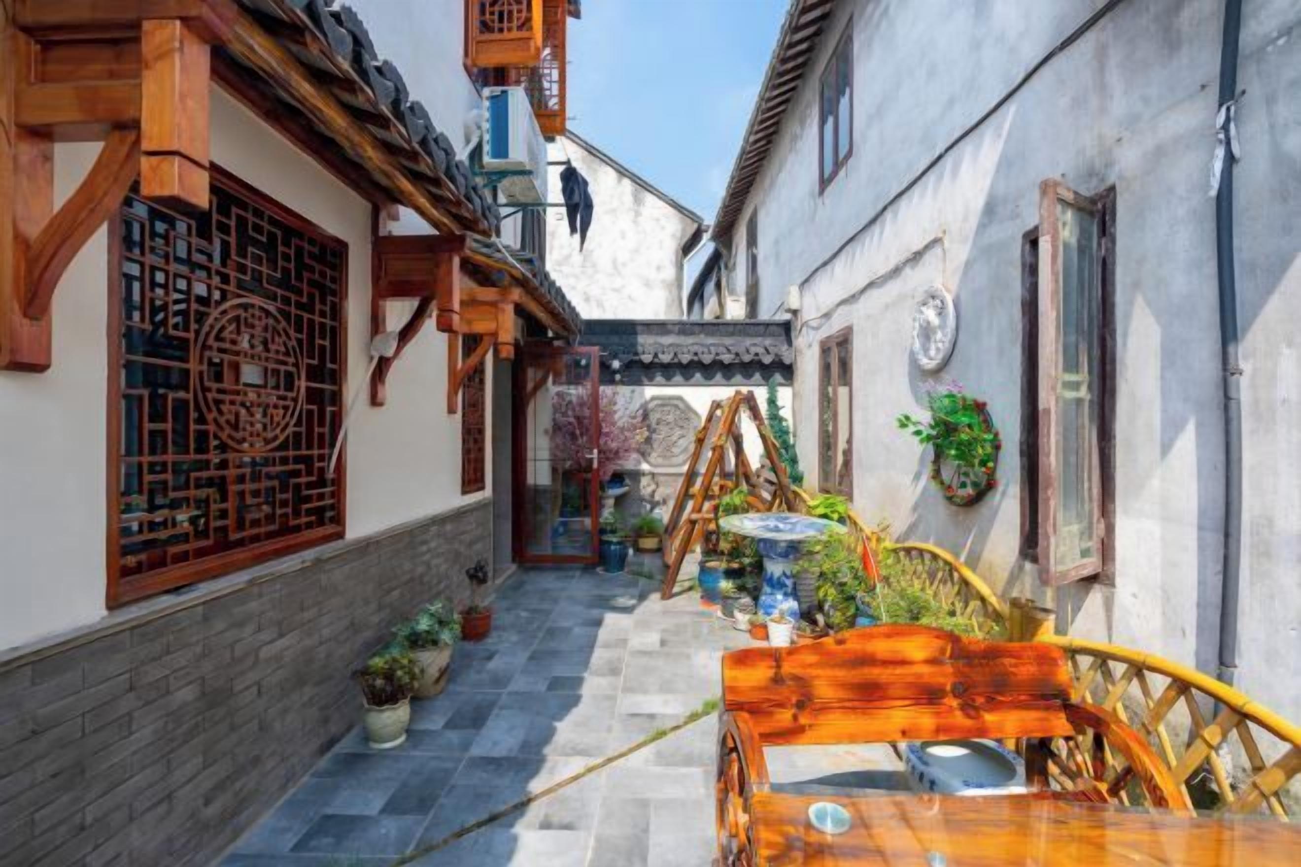 Une ruelle étroite aux bâtiments d’architecture traditionnelle, un banc en bois et des plantes en pot.