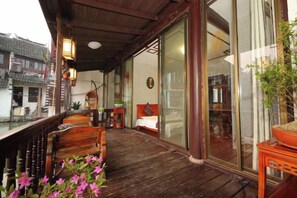 Un balcon en bois avec un lit, une chaise et un pot de fleurs.