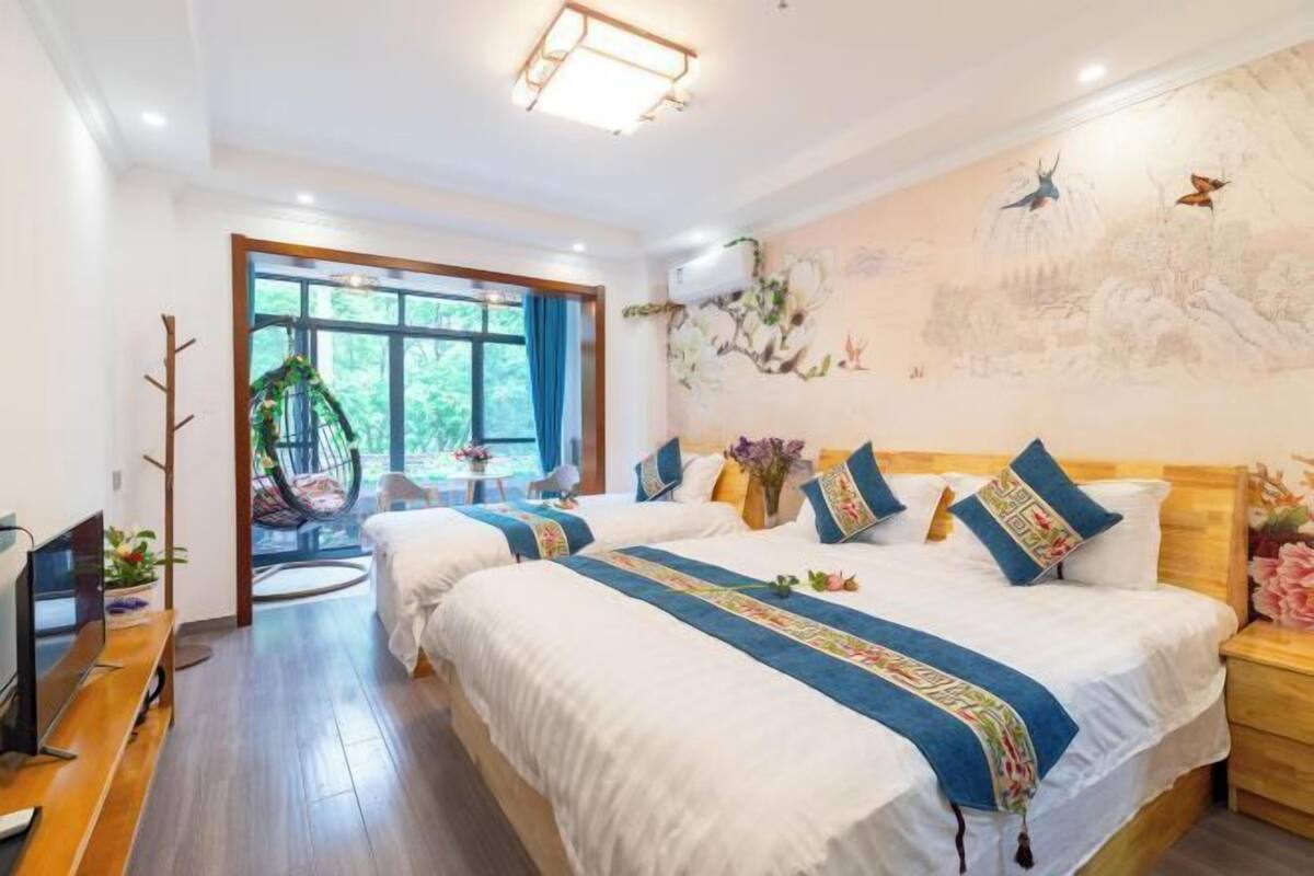 A hotel room with two beds, a TV, a wooden floor, a large window, and a mural on the wall.