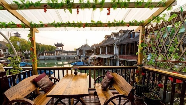 Een houten terras met banken en een tafel, met uitzicht op een waterpartij met traditionele gebouwen.