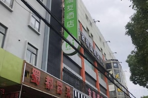 A hotel with multiple floors, a prominent green sign, and a clock tower. - Hi Inn (Shanghai Jinqiao Yanggao Middle Road) (Shanghai)