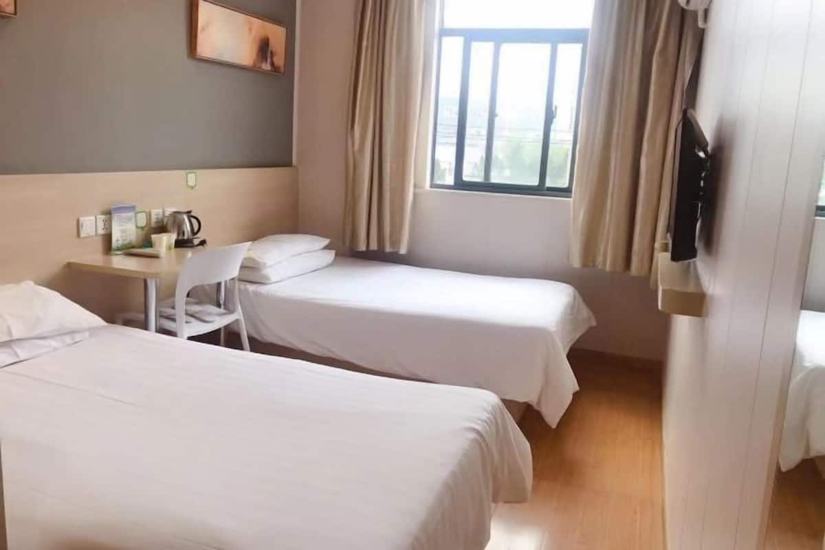 Une chambre d’hôtel avec deux lits, un bureau, une chaise, une télévision et une fenêtre avec des rideaux.