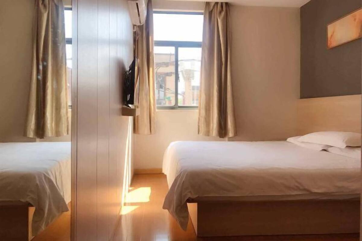 Une chambre d’hôtel avec deux lits, une fenêtre avec des rideaux et un tableau au mur.
