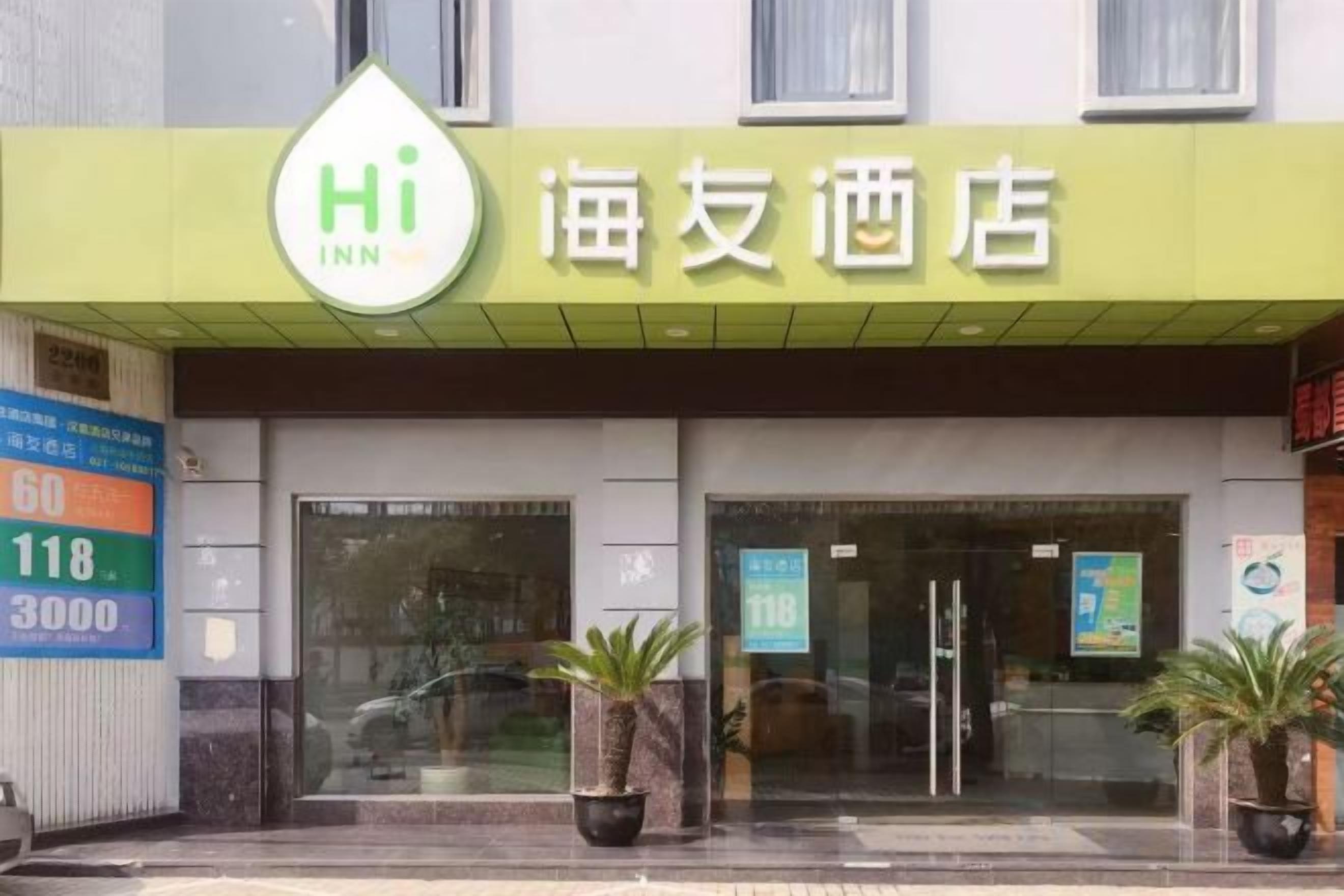 A hotel entrance with a green awning displaying the name 'Hi Inn' and Chinese characters. There are two potted plants in front of the entrance.