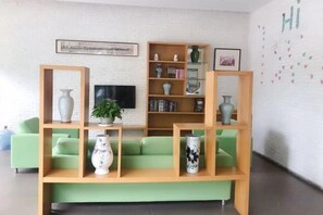 A living room with a green sofa, wooden shelves with decorative items, a flat-screen TV, and a white brick wall with a 'HI' sign. - Hi Inn (Shanghai Jinqiao Yanggao Middle Road) (Shanghai)