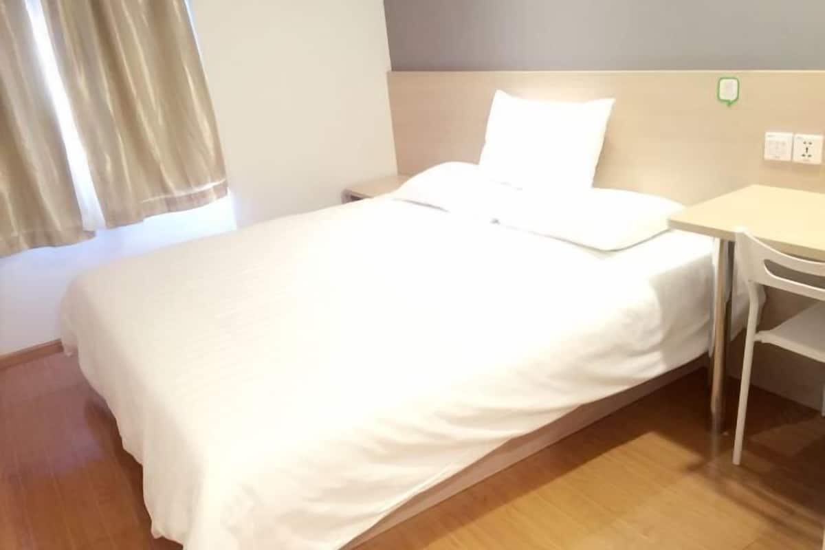 Un lit simple avec un matelas et des oreillers blancs, une petite table de chevet et un plancher en bois.