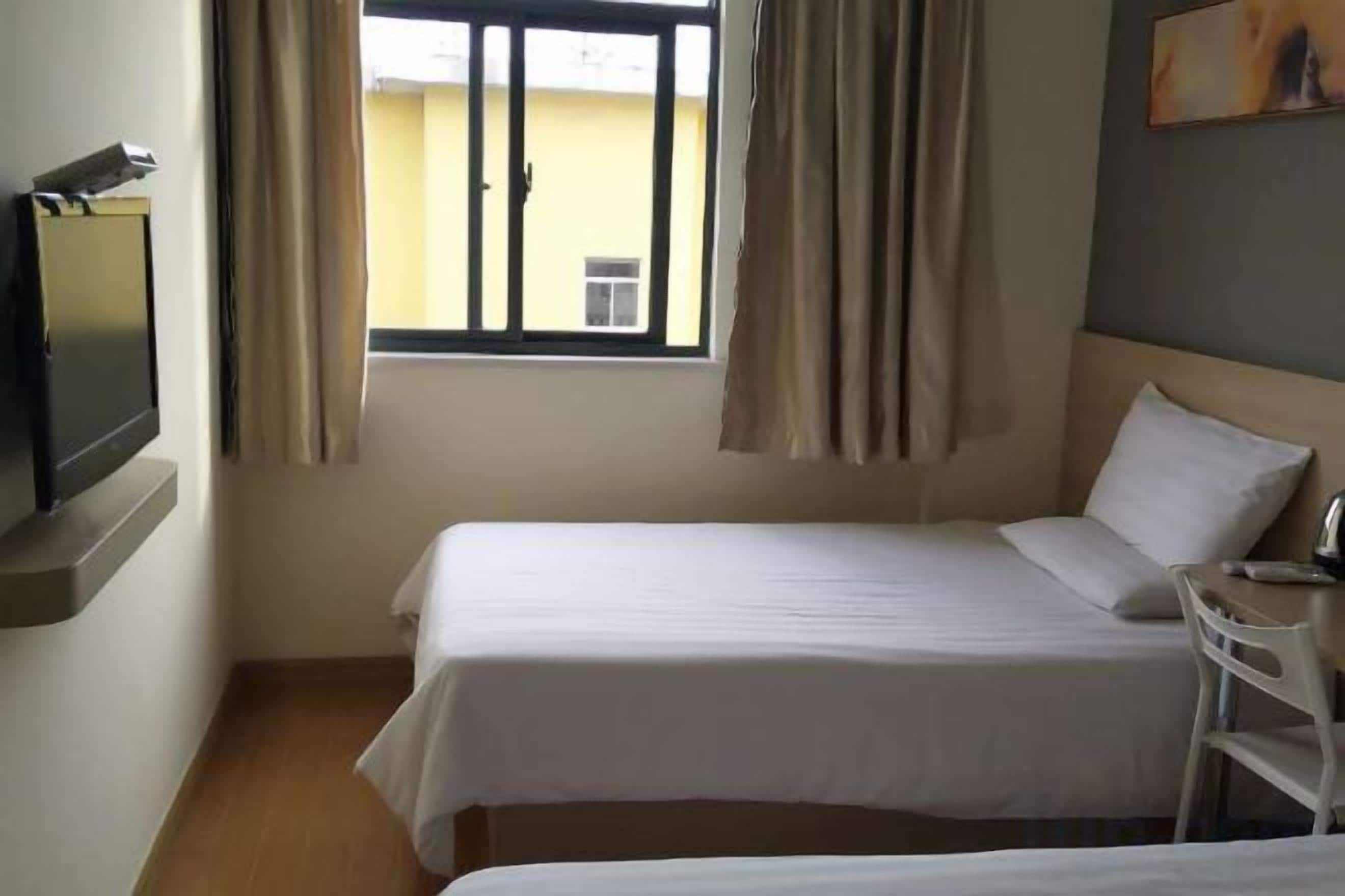 A hotel room with two beds, a TV, and a window with curtains.