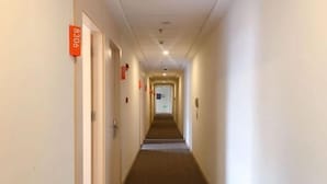 A hotel corridor with doors marked by orange signs, a carpeted floor, and a ceiling with recessed lighting. - Hi Inn (Shanghai Jinqiao Yanggao Middle Road) (Shanghai)