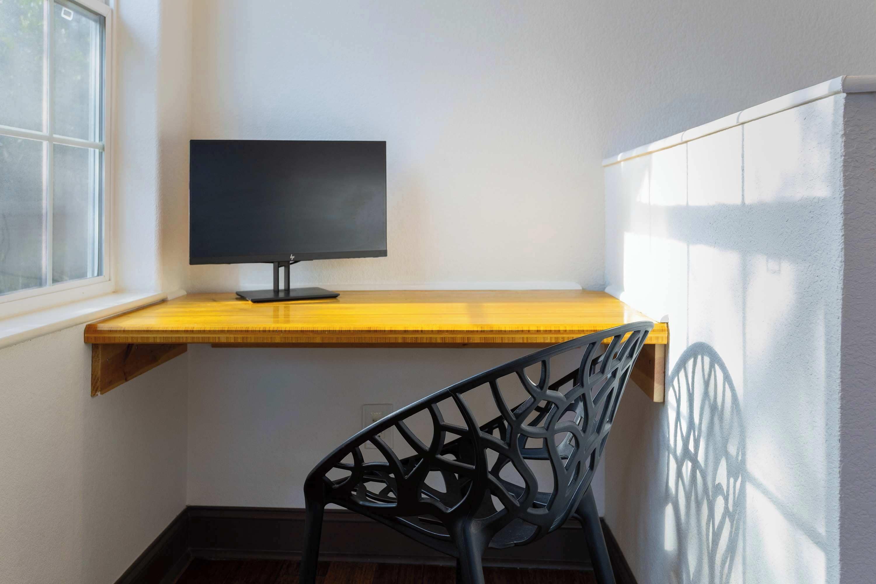 Un bureau d’angle avec un écran d’ordinateur, une chaise et une fenêtre.