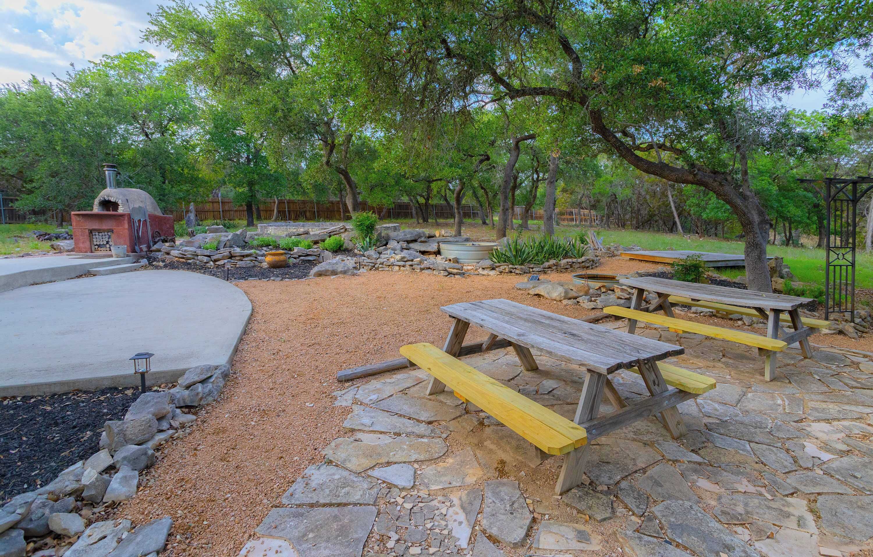 A patio area with stone flooring, wooden picnic tables, and a barbecue grill.