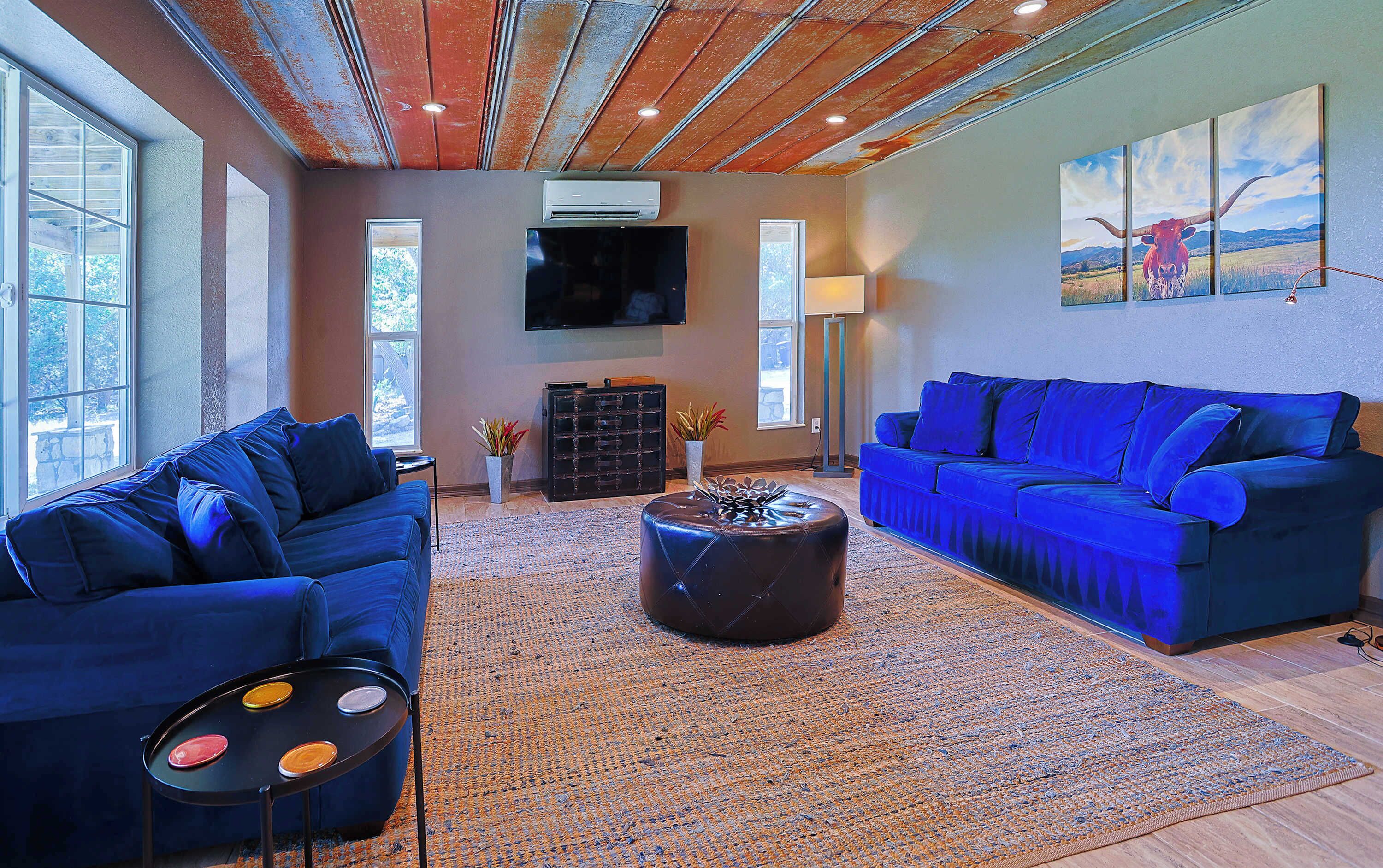 A modern living room with blue sofas, a coffee table, and a flat-screen TV mounted on the wall.