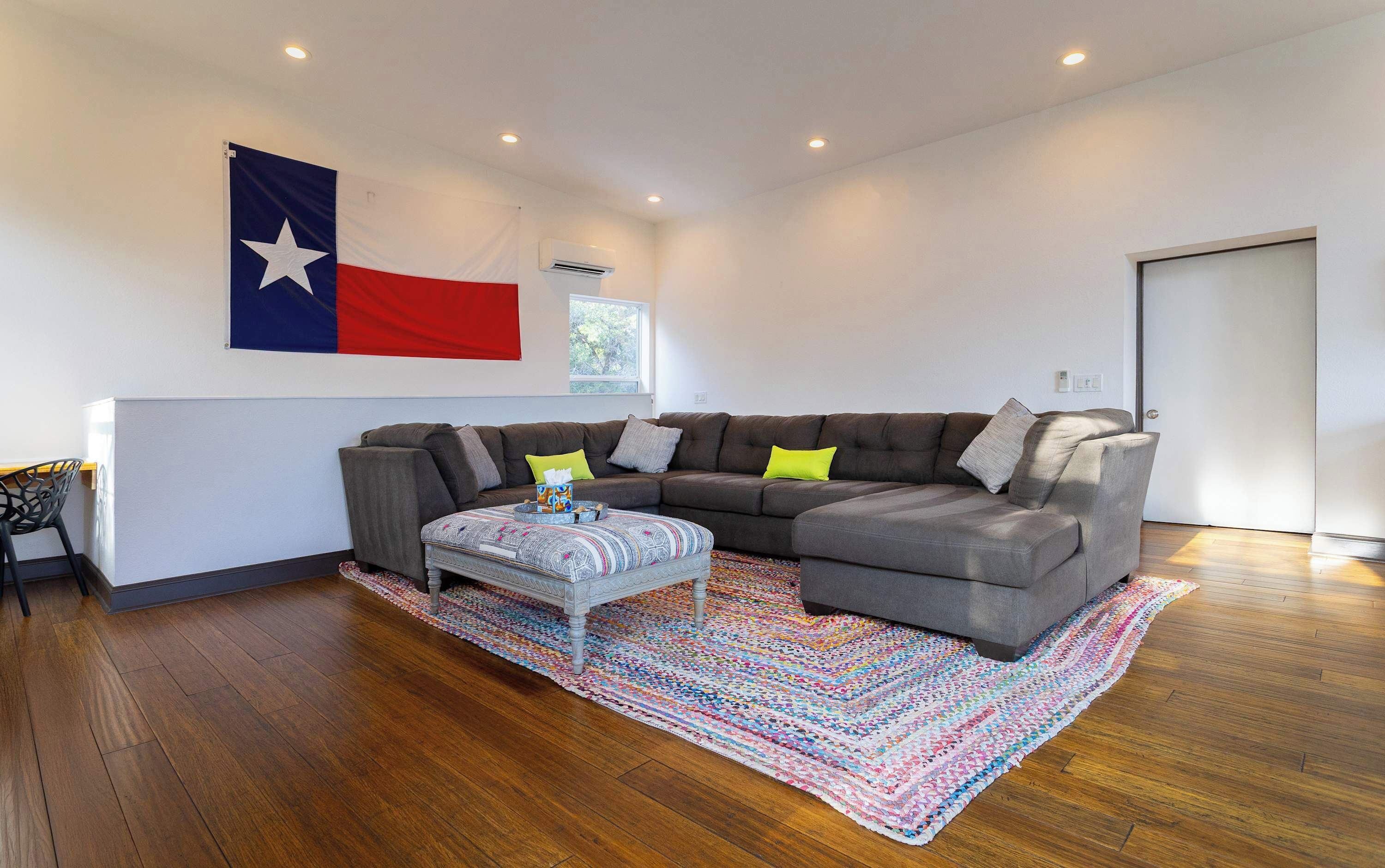A modern living room with a sectional sofa, a patterned ottoman, and a Texas flag on the wall.