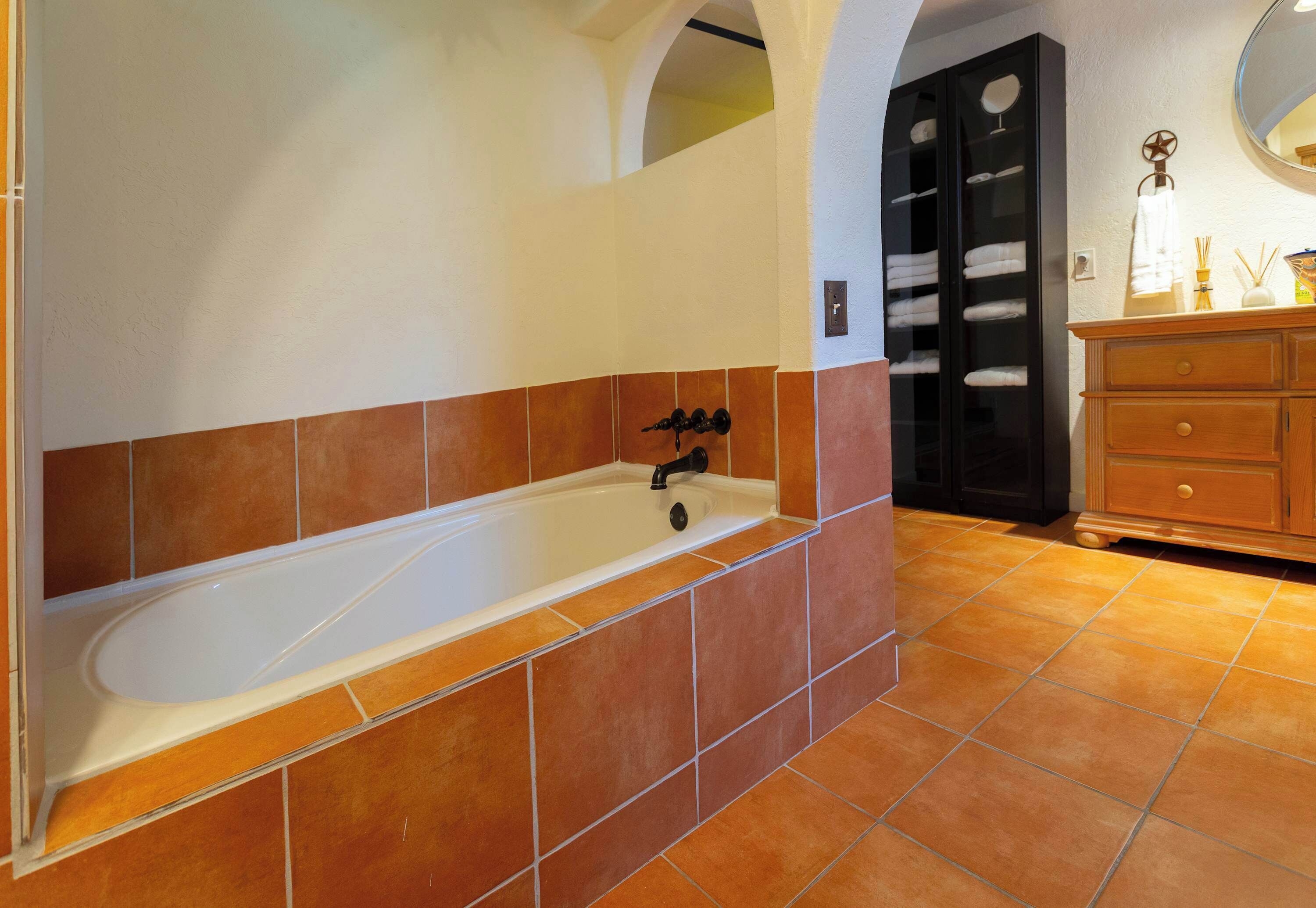 A bathroom with a bathtub, tiled walls, a wooden vanity, and a towel rack.