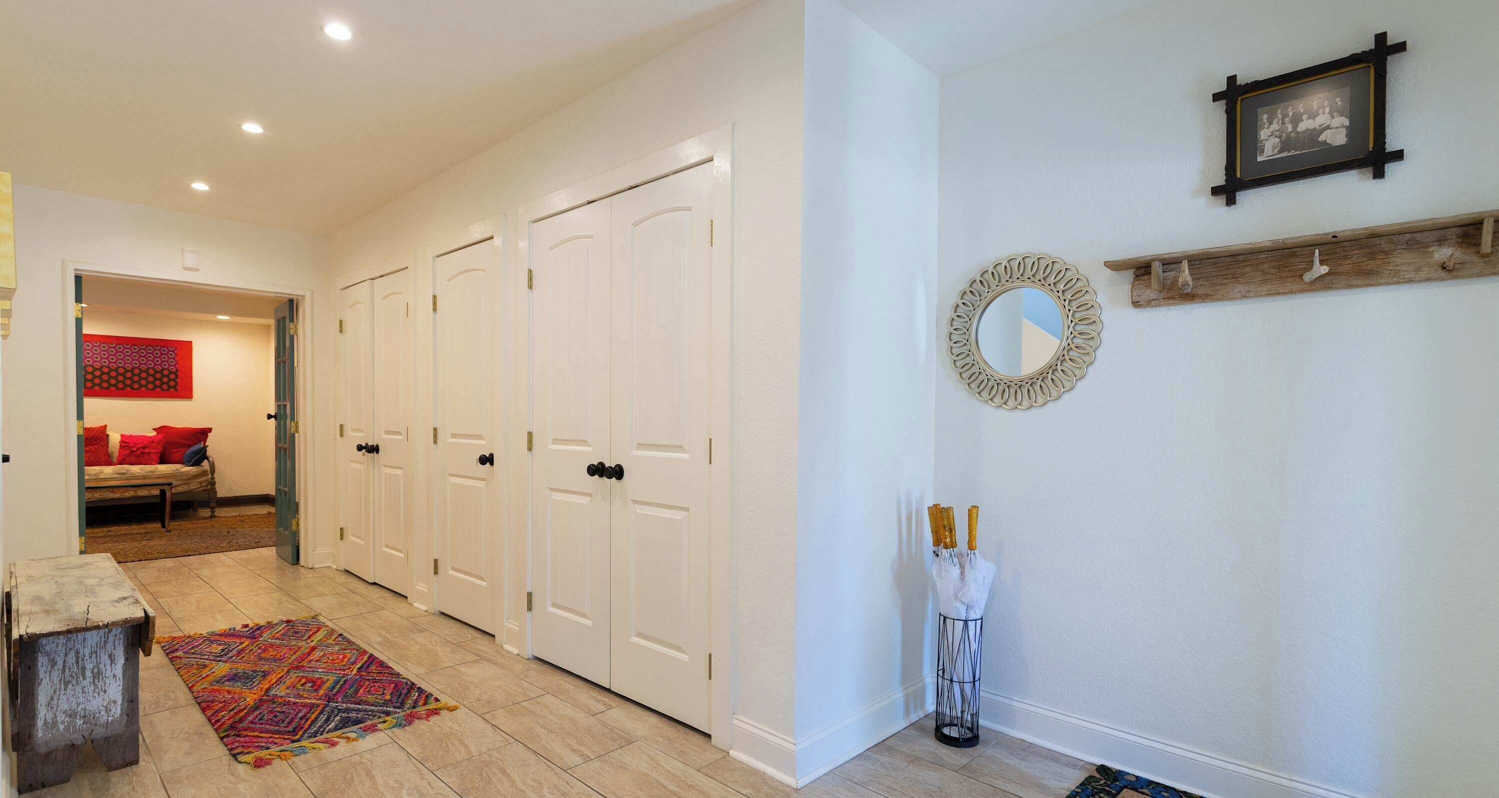 A hallway with white doors, a patterned rug, a bench with red cushions, and a mirror on the wall.