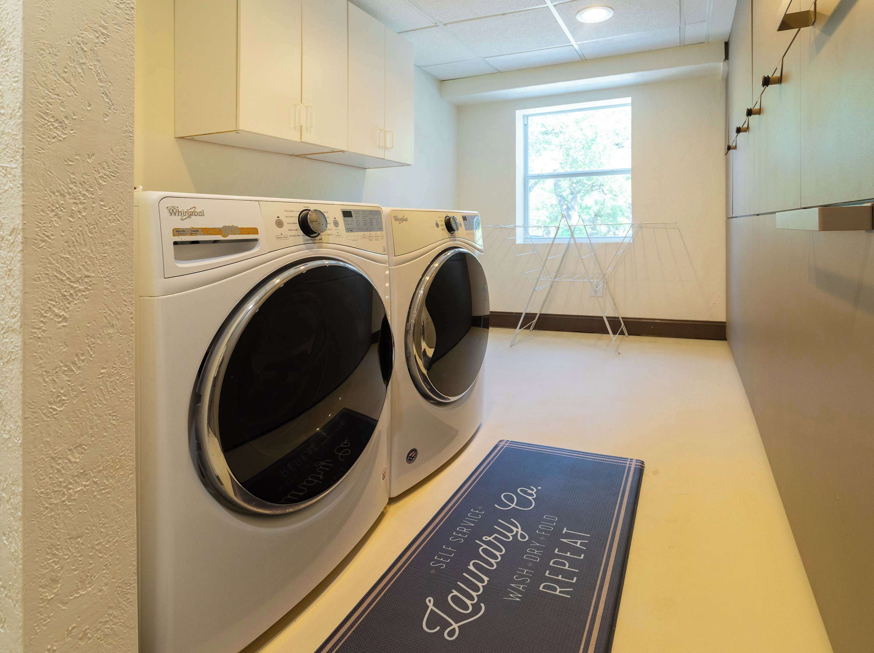 A laundry room with two front-loading Whirlpool washers, a drying rack, and a mat with "Laundry Co." branding.