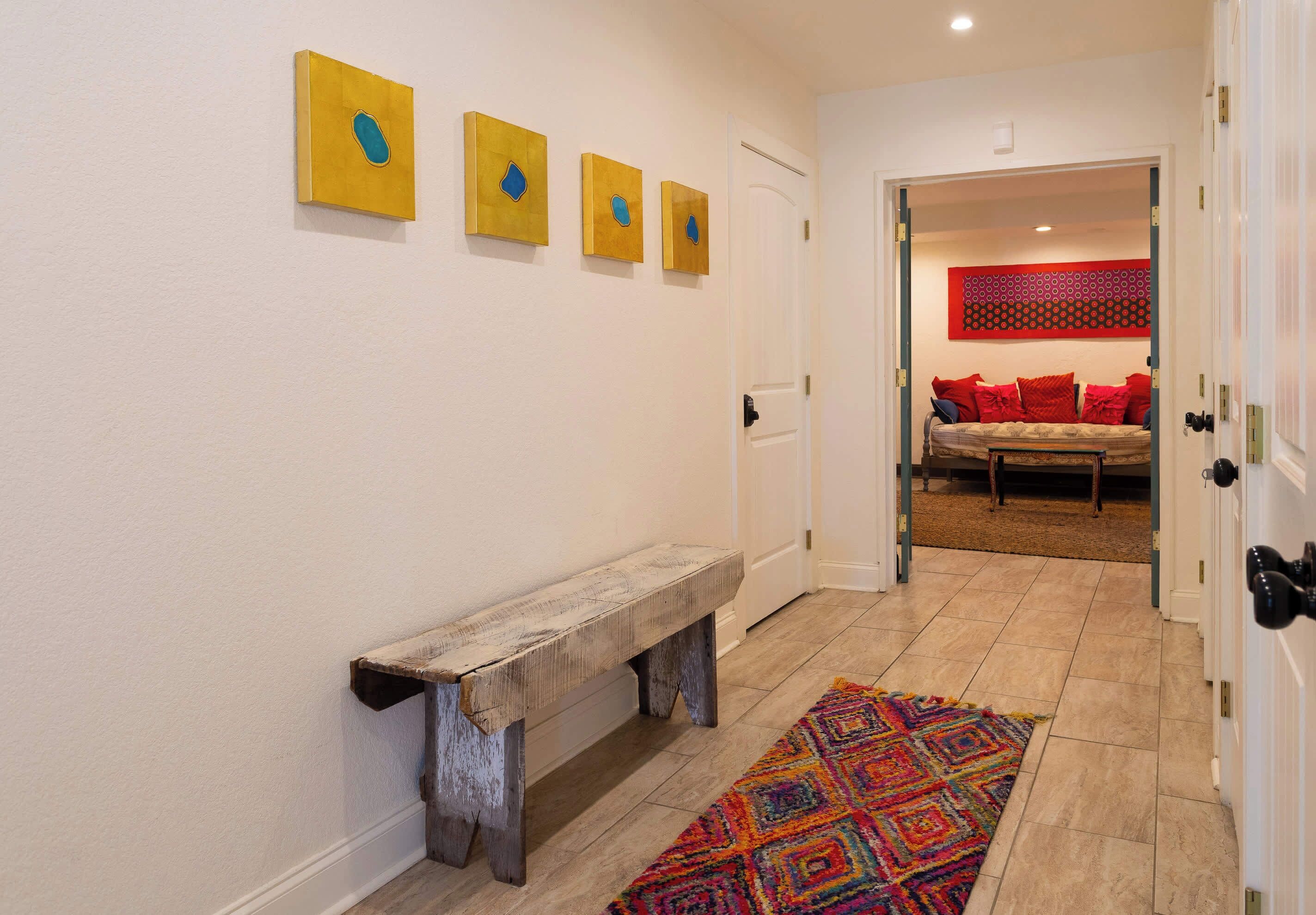 A hallway with a wooden bench, a colorful rug, and three framed artworks on the wall.
