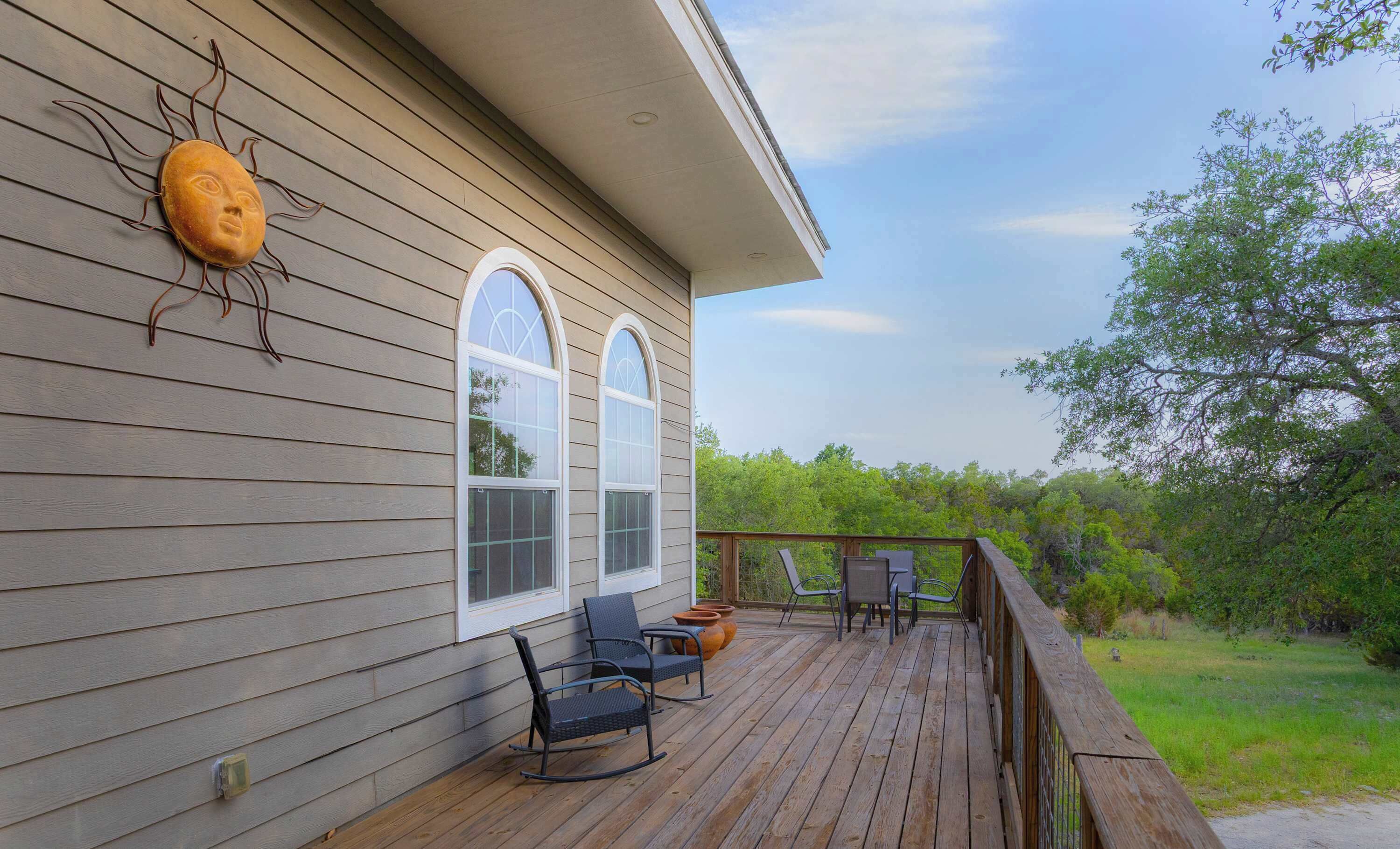 A wooden deck with outdoor furniture, a large arched window, and a decorative sun-like sculpture on the wall.