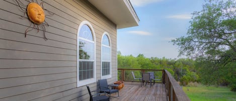 A wooden deck with outdoor furniture, a large arched window, and a decorative sun-like sculpture on the wall.