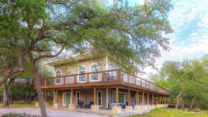 A two-story house with a porch, stone steps, and a covered patio area. - Willie's Hill Country Hideaway - Stay for 8 With Hot Tub & Fire Pit (Wimberley)