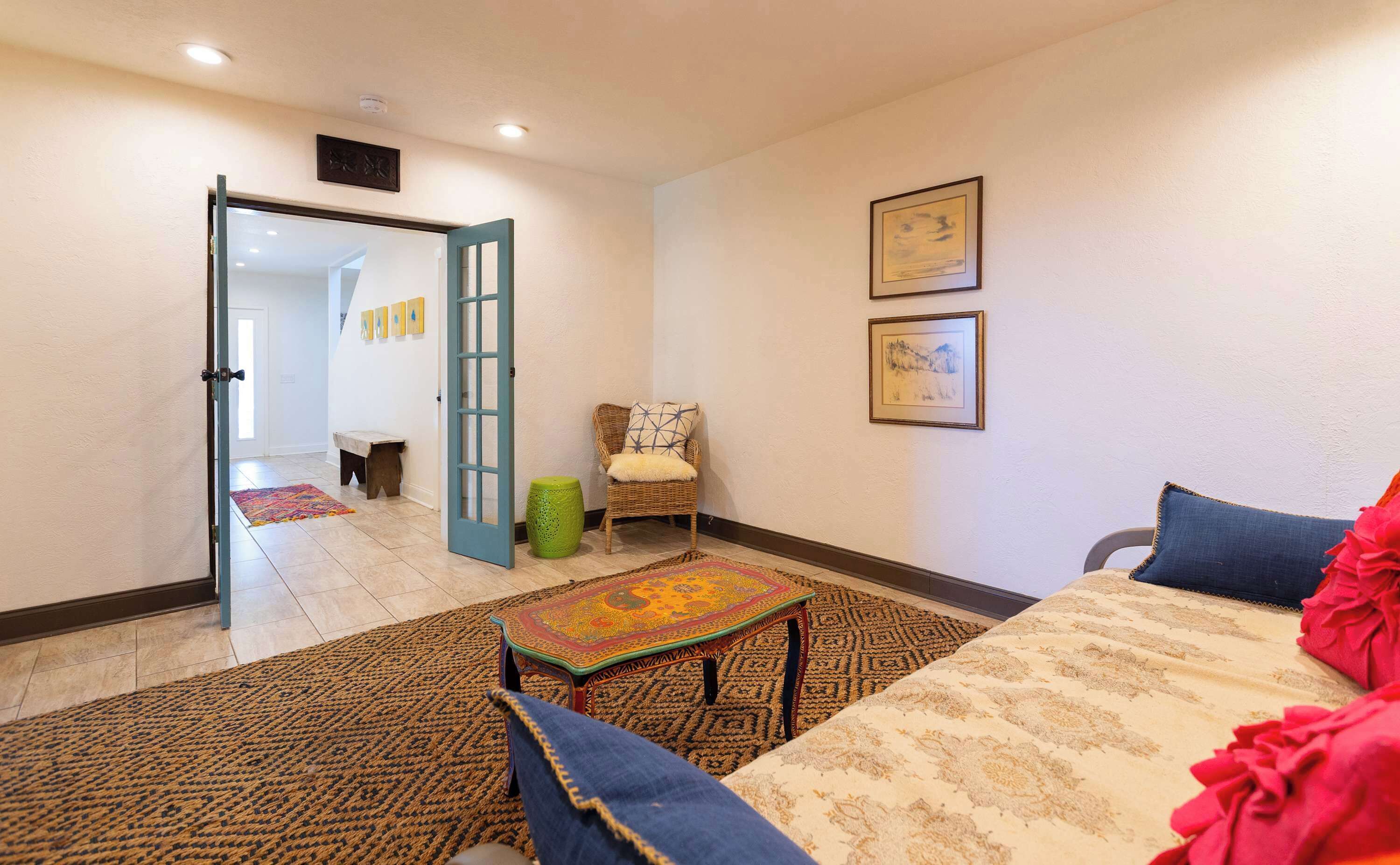 A room with a sofa, a patterned rug, a small table, and a chair. There is a door leading to another room.