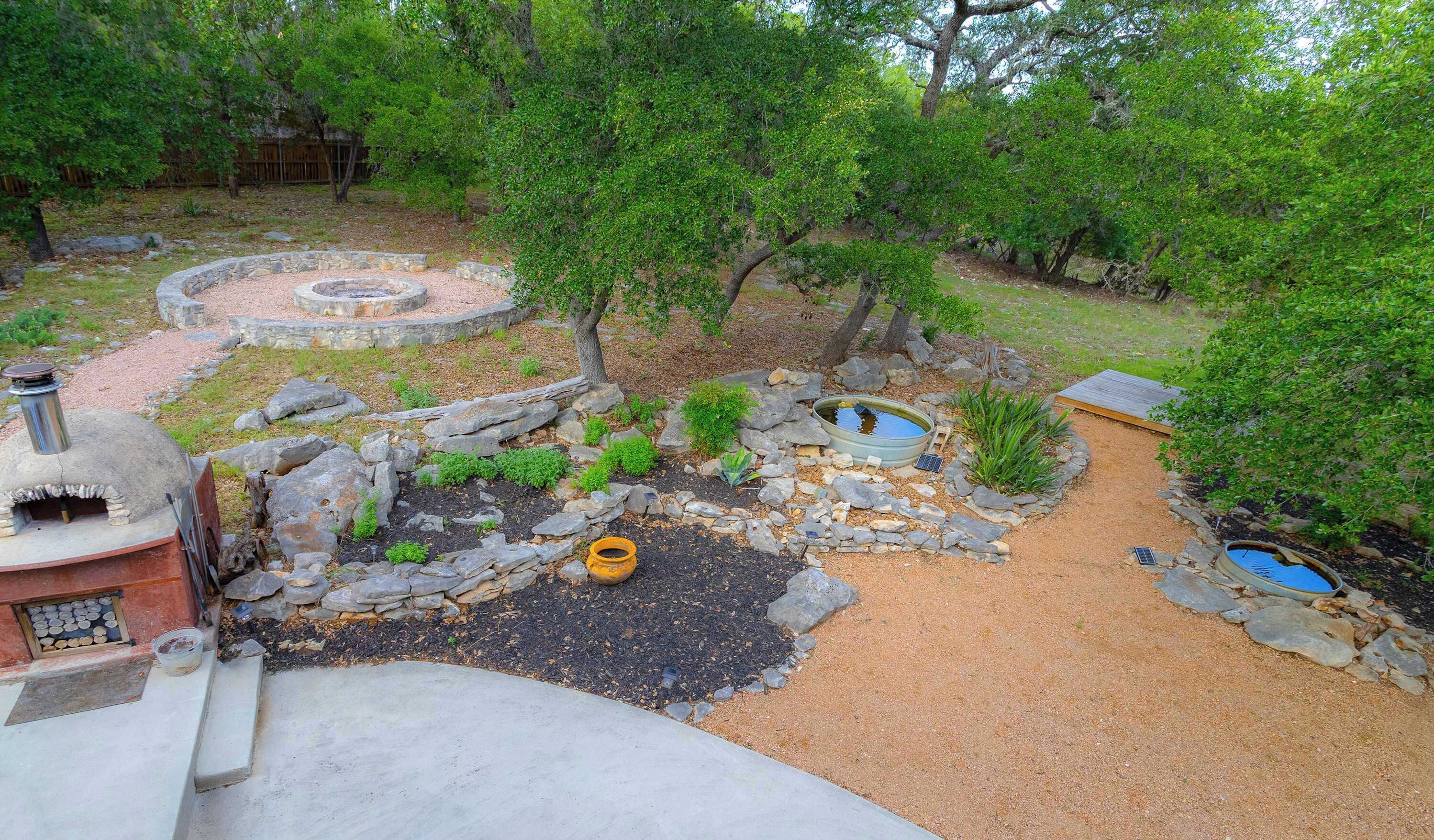 Un jardín con un hogar de piedra, un estanque y una pequeña construcción de madera.