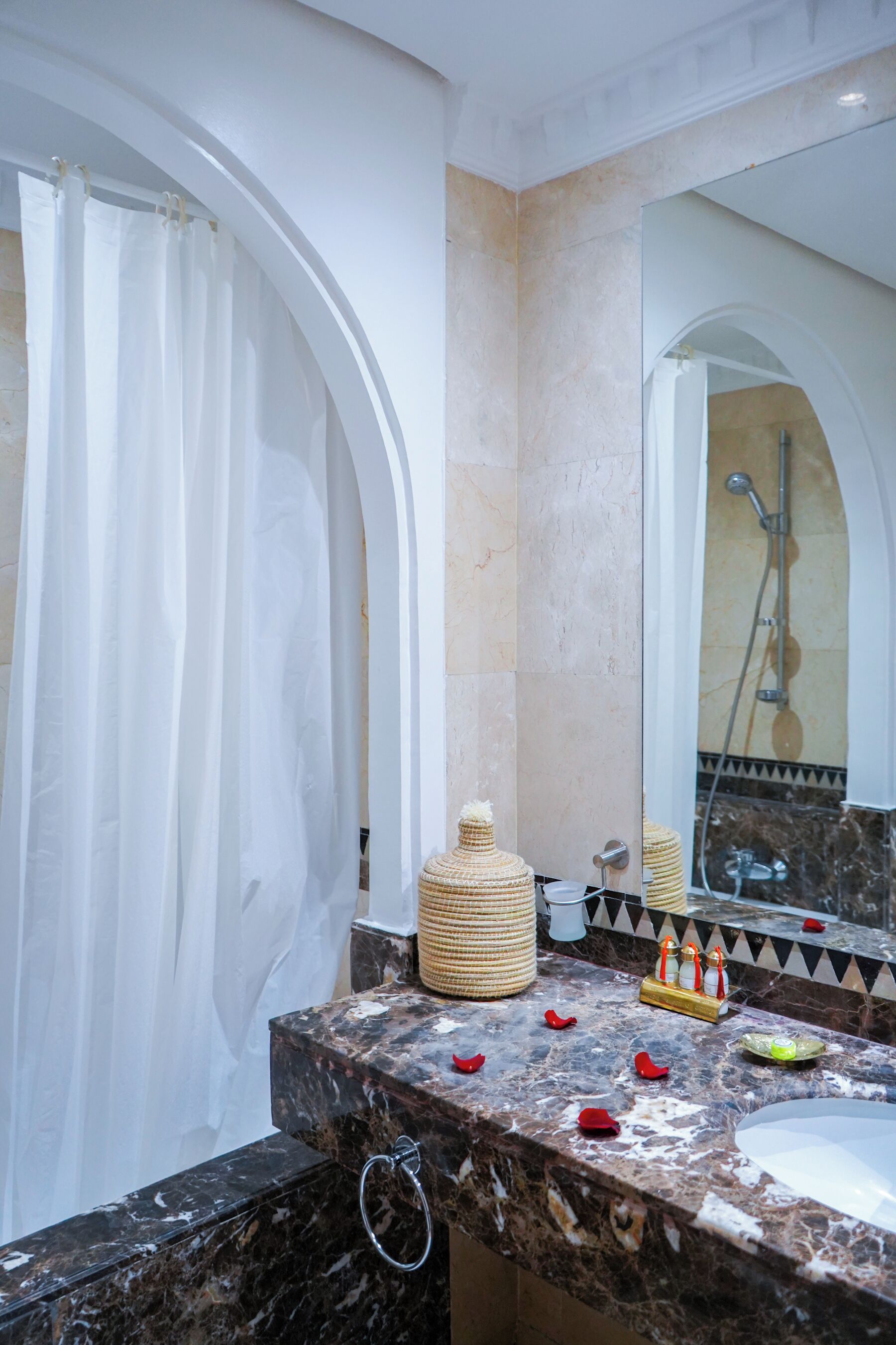 A bathroom with a marble sink, a shower, and a large mirror.