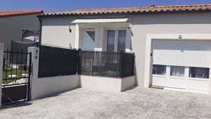 Una casa de dos plantas con garaje, entrada protegida por un portón y un patio con baldosas.