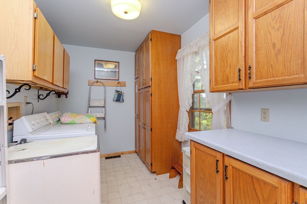A compact kitchen with wooden cabinets, a washing machine, and a small window with a curtain.
