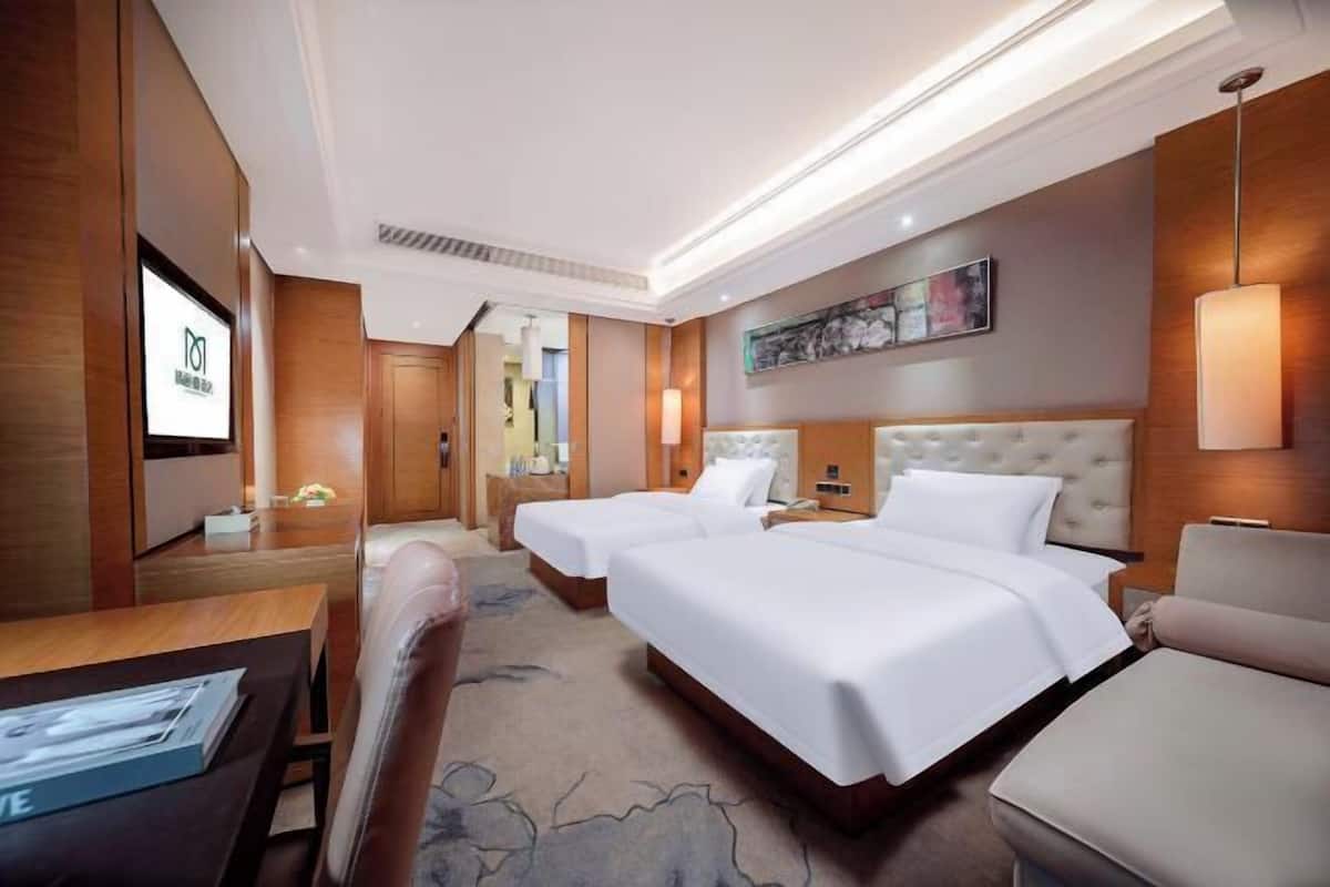 A hotel room with two beds, a desk, a chair, a TV, and a painting on the wall.