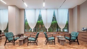 A room with a wooden herringbone floor, large windows with white curtains, and teal upholstered chairs around small round tables. - Mastery 101 Hotels (Nanning)
