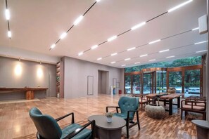 A spacious lobby with a wooden floor, seating area with chairs and tables, and large windows offering a view of the outdoors. - Mastery 101 Hotels (Nanning)