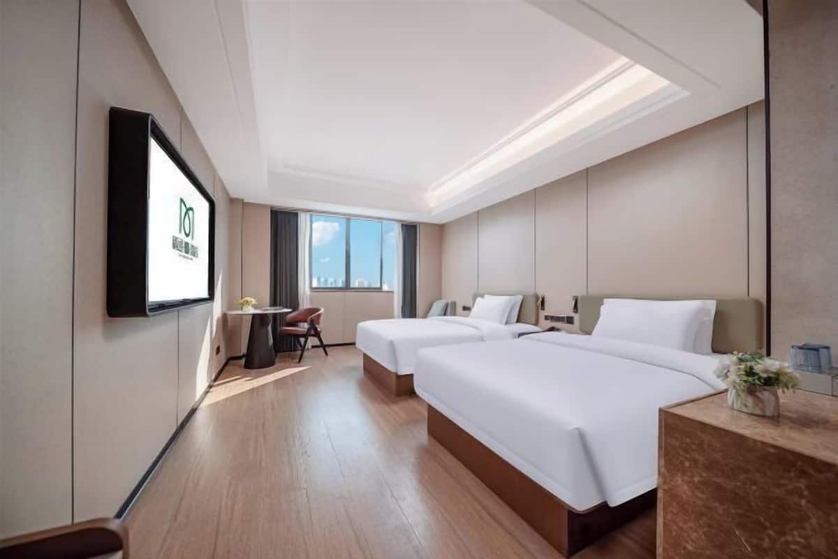 A hotel room with two beds, a desk, a chair, a TV, and a window.