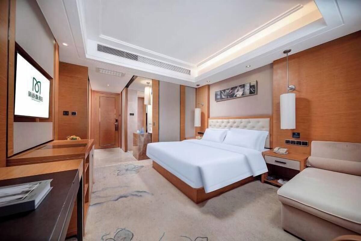 A hotel room with a bed, bedside table, lamp, and a desk with papers.