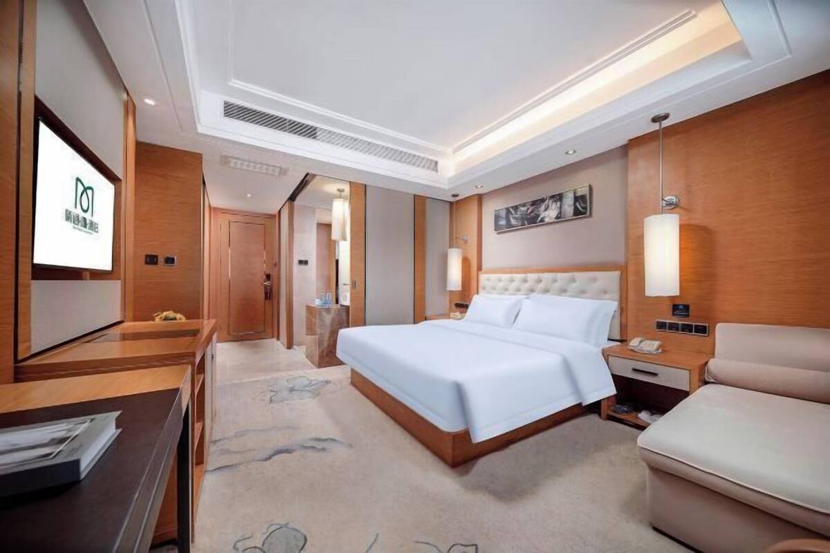 A hotel room with a bed, bedside table, lamp, and a TV screen displaying a logo.