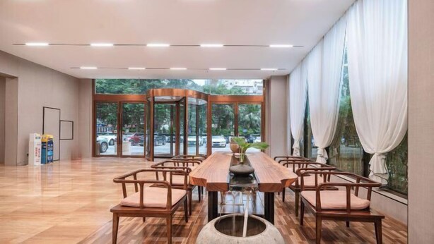 A spacious room with a long wooden table and chairs, large windows with white curtains, and a view of the outside. - Mastery 101 Hotels (Nanning)