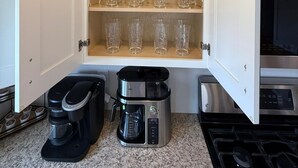 Een keuken met een inbouwkast met wijnglazen en tumblers, een Keurig koffiezetapparaat en een koffiepot.