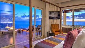 Une chambre d’hôtel avec un grand lit, une télévision, une chaise, une petite table et une vue sur l’océan.