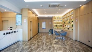 Zona de recepción de un hotel con suelo de mármol, paneles de madera, mostrador de recepción, área de asientos y una estantería.