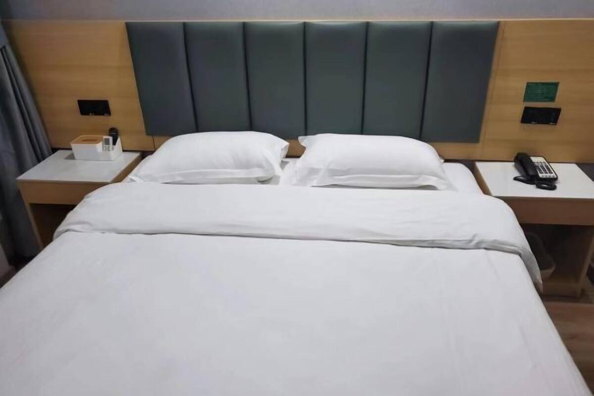 Una habitación de hotel con una cama, dos mesitas de noche, cabecera y teléfono.