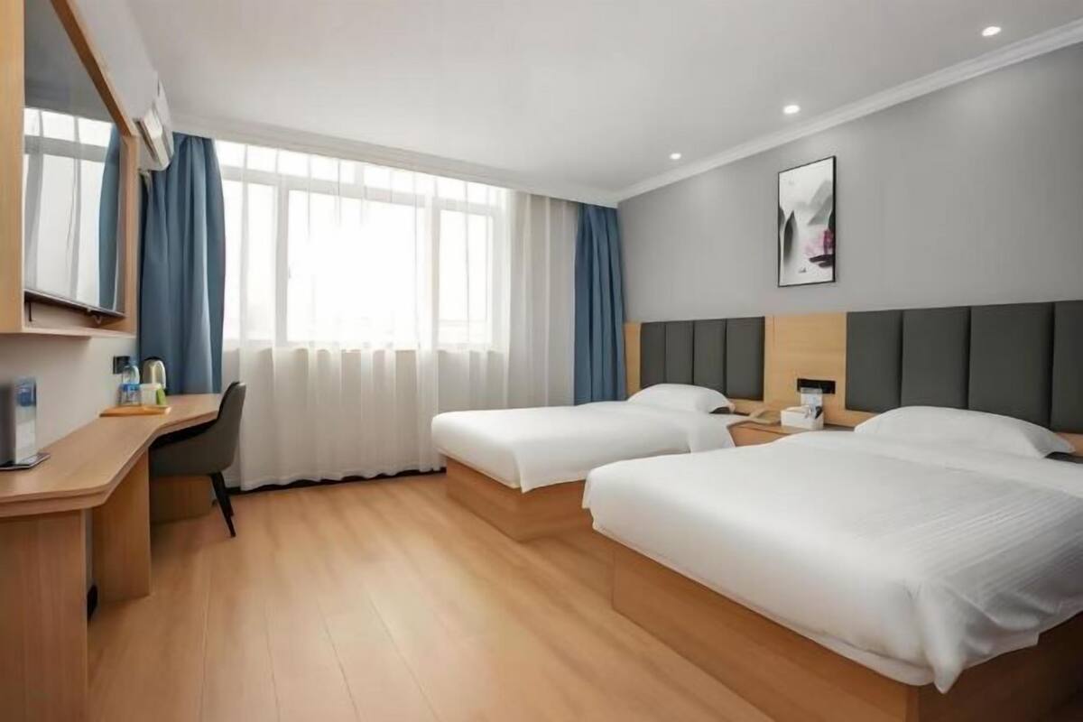 Habitación de hotel con dos camas, un escritorio, una silla, un televisor y una ventana con cortinas.